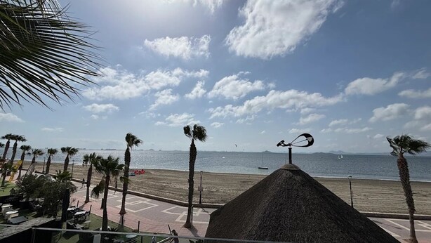 A beach view with palm trees, a thatched-roof structure, and a clear sky. - Spacious house just steps from the beach 2 min walk (Los Alcázares)