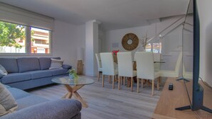 A modern living room with a sofa, a glass coffee table, and a dining area with chairs and a table. - Spacious house just steps from the beach 2 min walk (Los Alcázares)
