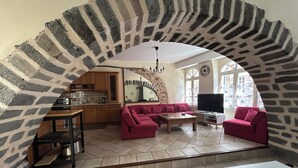 A living room with a stone archway, a kitchen area, and a dining table.
