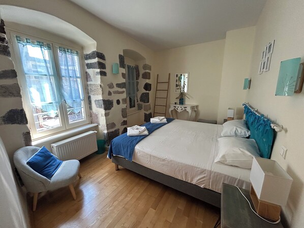 A bedroom with a stone wall, a bed with white bedding, a chair with a blue cushion, and a window with curtains. - 6 Bedroom Private vacation home in Brioude (Brioude)