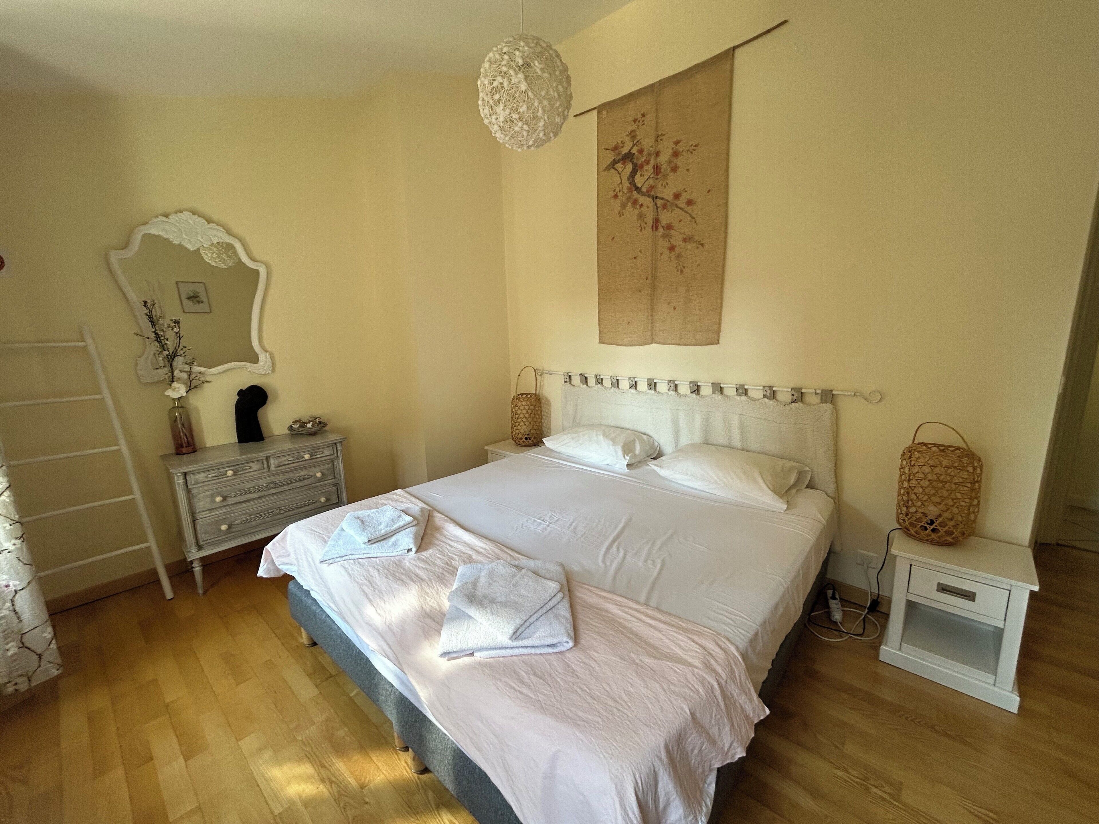 A neatly arranged bedroom with a bed, bedside tables, a dresser, and a hanging light fixture.