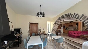 A spacious living area with a dining table and chairs, a kitchen, a staircase, and a red sofa.