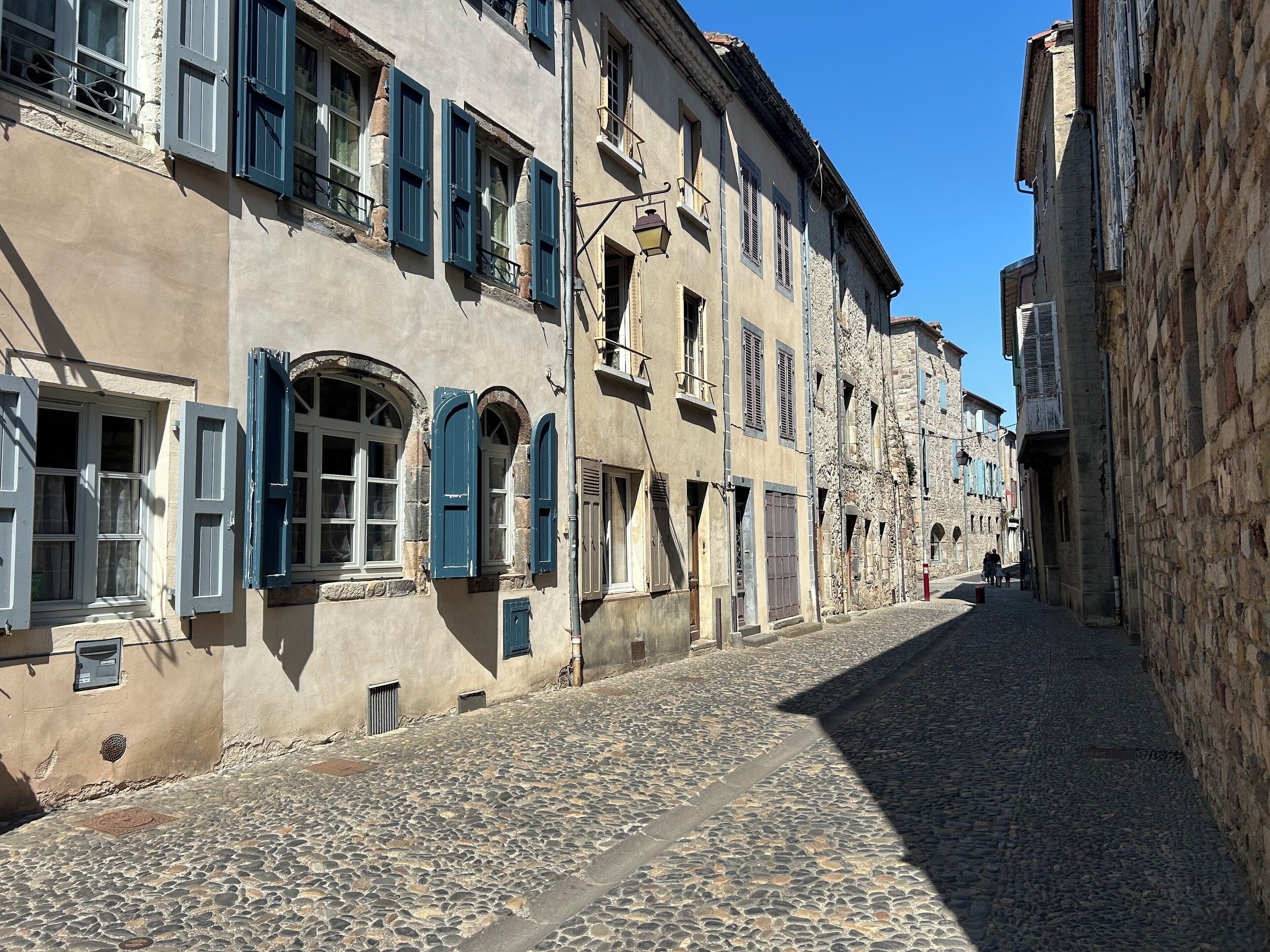 Eine enge Kopfsteinpflasterstraße, gesäumt von historischen Gebäuden mit Steinfassaden und blauen Fensterläden.
