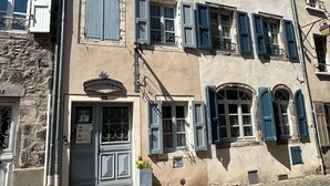 A multi-story building with stone facade, multiple windows with shutters, and a cobblestone street.