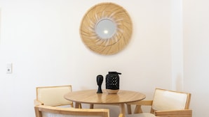 Un tavolo rotondo in legno con due sedie, un vaso nero e uno specchio intrecciato appeso al muro.