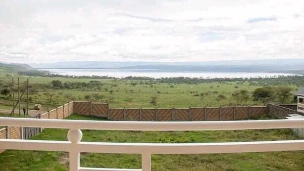 A view from a balcony overlooking a grassy landscape with a distant body of water and a cloudy sky. - Lux Suites Naxity Apartments Nakuru (Nakuru)