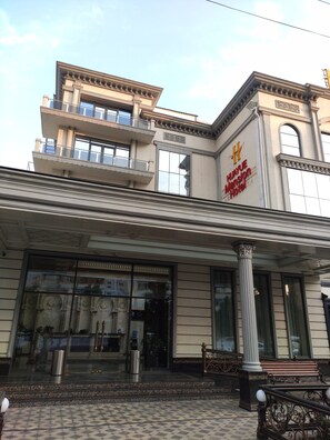 A building with a classical architectural style, featuring a prominent entrance with a large glass facade, columns, and a balcony. - Huayue Mansion Hotel (Tashkent)