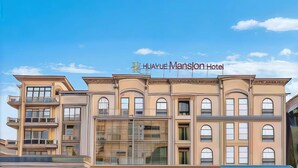 Un hotel a più piani con un design architettonico classico, caratterizzato da ampie finestre e una segnaletica ben visibile per Huayue Mansion Hotel.