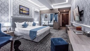 Una camera d'albergo moderna con un letto grande, una scrivania, una sedia e un bagno visibile tramite una porta in vetro.