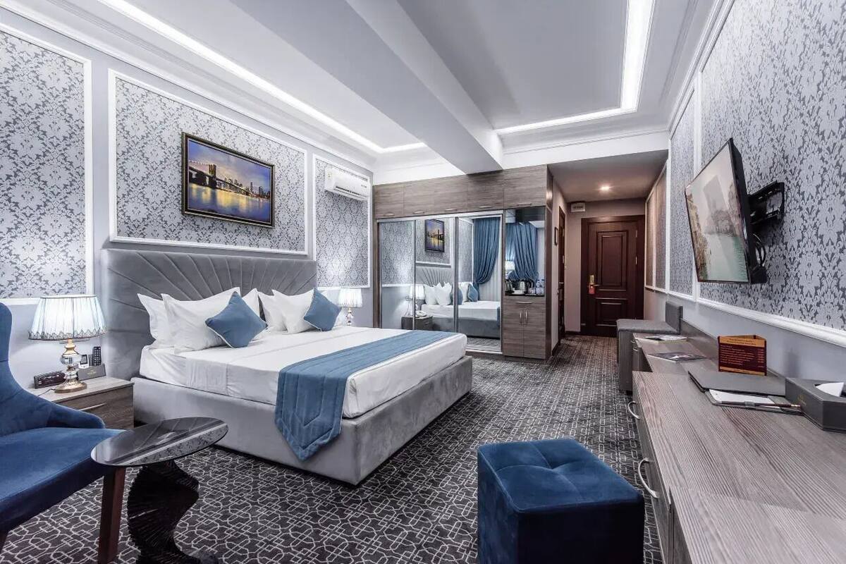 Moderni hotellihuone, jossa on suuri sänky, työpöytä, tuoli ja kylpyhuone, joka näkyy lasiovesta.