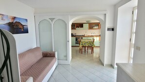 A living room with a sofa, a dining area with a table and chairs, and a kitchen with cabinets and appliances.