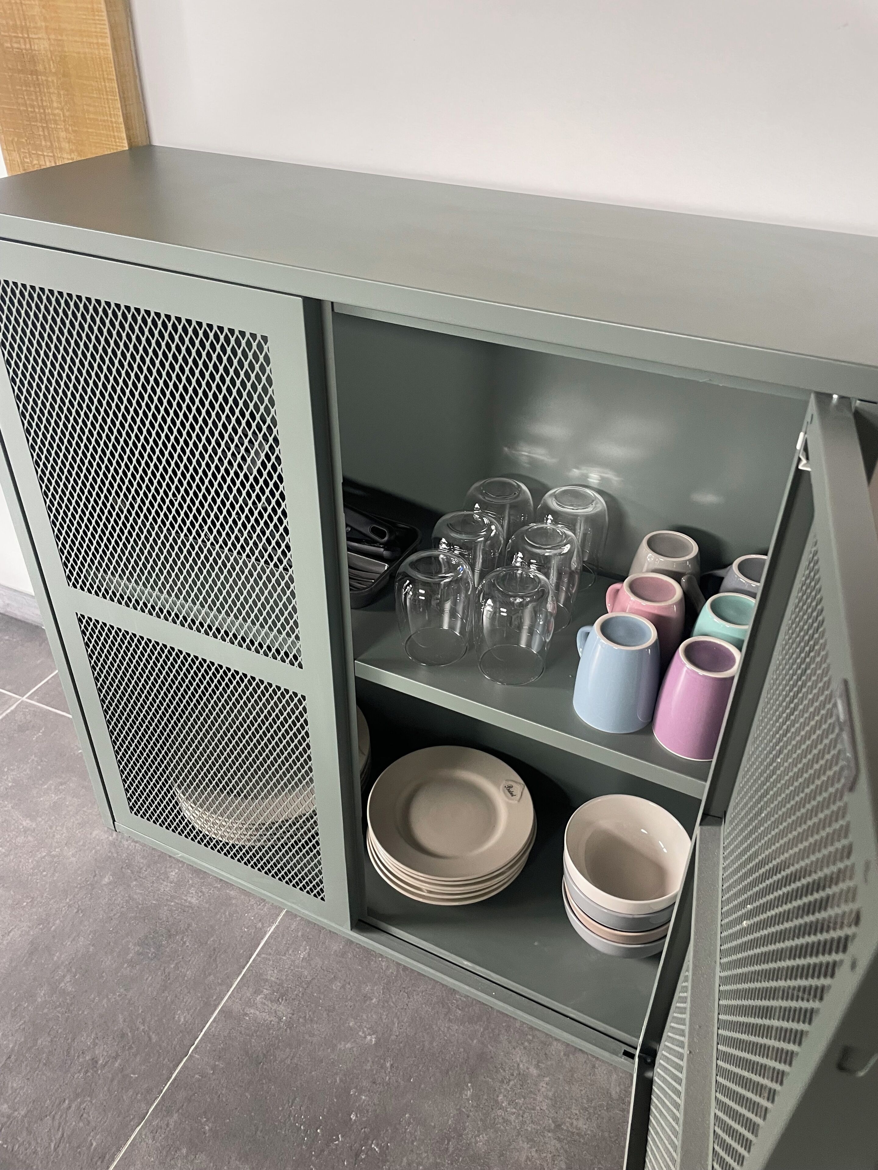 Een metalen kast met planken vol glaswerk, borden en bekers.
