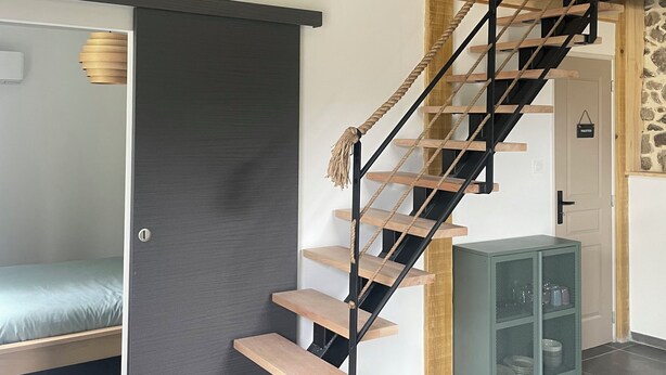 Una escalera con escalones de madera y barandillas negras, que lleva a una zona superior con un televisor fijado al techo.