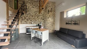 Una cocina moderna con pared de piedra, escalera de madera y sofá gris.