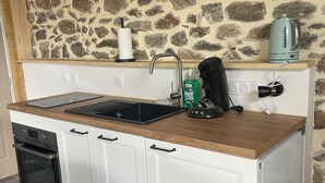 Una cocina compacta con pared de piedra, horno empotrado, lavamanos y tetera sobre la encimera.