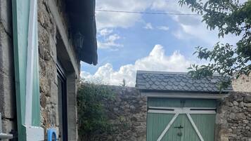 Une terrasse avec deux chaises en osier noir et une petite table, un mur de pierre et, au fond, une porte verte.