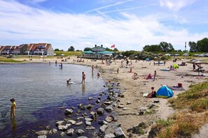 A beach with people swimming and relaxing, a tent, and a building with a flag.