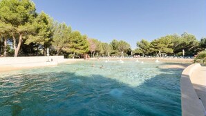 A swimming pool surrounded by trees and a beach area with people and umbrellas. - 2 Room Apartment for 4 People (Mallemort)