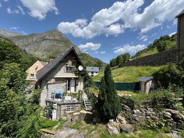 A stone house with a sloped roof, a satellite dish, and a small outdoor seating area.