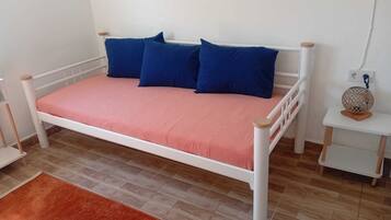 Uma cama de solteiro com estrutura branca e colchão rosa, acompanhada por quatro almofadas azuis.