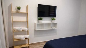 A hotel room with a bed, a TV mounted on the wall, a wooden shelf with towels, and a small plant. - Kavala Hotel Bodrum (Bodrum)