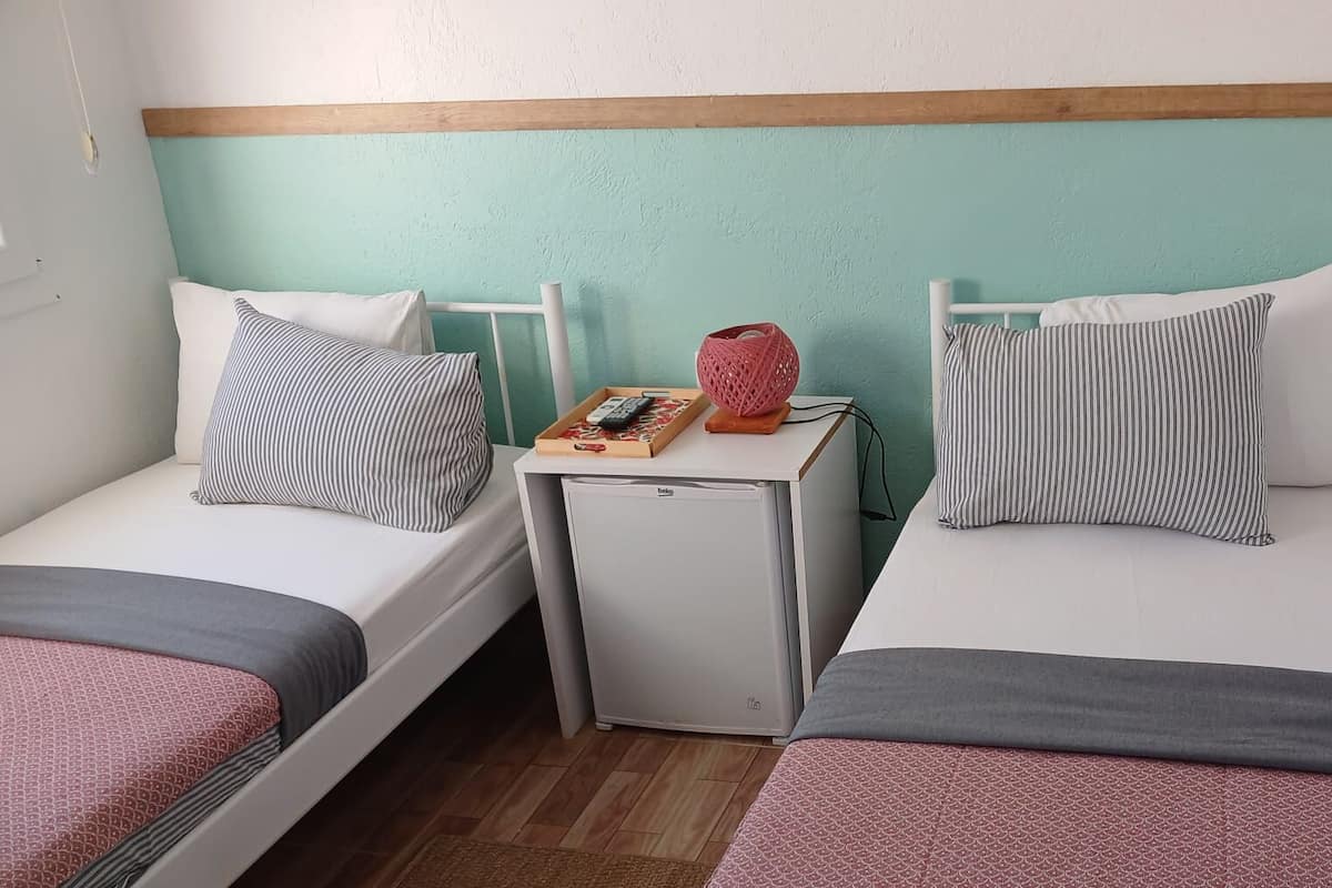 Ein Doppelzimmer mit zwei Einzelbetten, einem kleinen Nachttisch mit Lampe und einem Fenster.