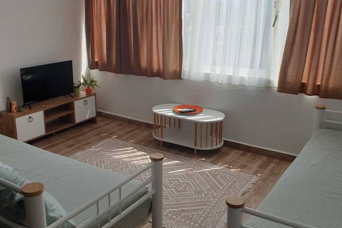 Ein Zimmer mit zwei Betten, einem Fernseher, einem kleinen Tisch und einem Fenster mit Vorhängen.