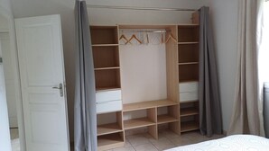 Armadio a muro con scaffali multipli e spazio per appendere, una porta e tende grigie.