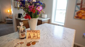 Un plan de travail de cuisine orné d’un vase de fleurs, d’un pot de compote de pommes et d’une carte avec un message.