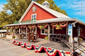 Ein rot gestrichenes Bauernhaus mit einem Schild, auf dem "Farm Market" steht, und einer Bühne mit Stühlen und einem Tisch.