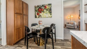 Un coin repas avec un buffet en bois, une table dressée et des chaises. Un tableau représentant des fruits est accroché au mur.