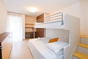 Una camera con un letto a castello, una scrivania, una sedia, un tavolino e una finestra con tende.