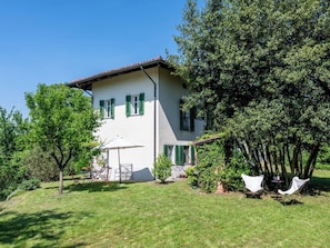 Una casa de dos pisos con fachada blanca, contraventanas verdes y un patio con muebles de exterior.