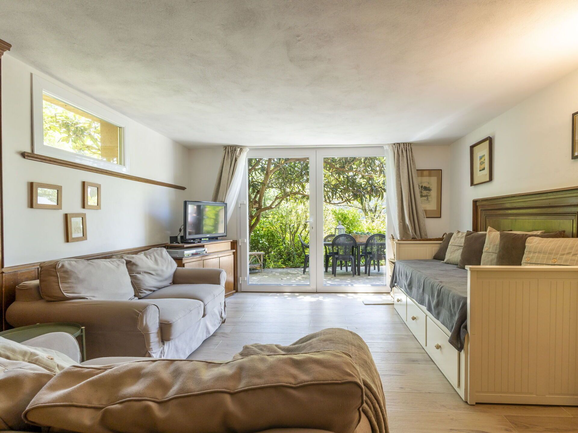 A cozy room with a sofa, a bed, a TV, and a sliding glass door leading to an outdoor area with chairs.