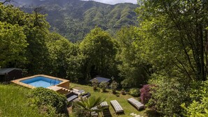 Ein Poolbereich mit Liegestühlen und einer Holzterrasse, umgeben von üppiger Vegetation und Bergen im Hintergrund.