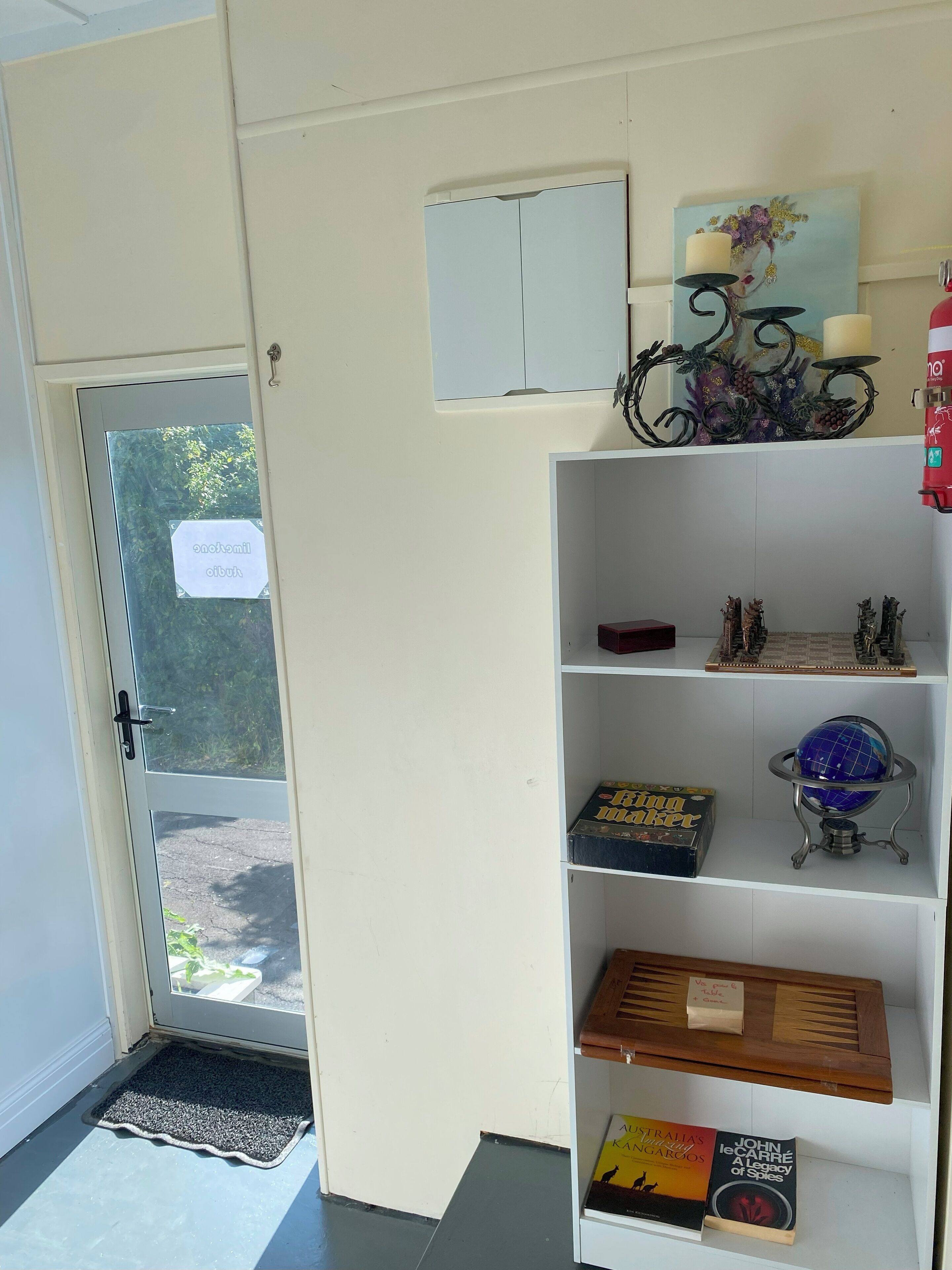 Une pièce avec une porte blanche, une petite étagère avec des livres et un globe terrestre, et un objet décoratif accroché au mur.