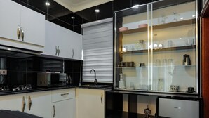 Een moderne keuken met witte kasten, een zwart aanrecht en een vitrinekast met verschillende spullen.