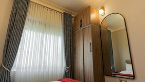 Een slaapkamer met een bed, een kledingkast, een spiegel en een raam met gordijnen.