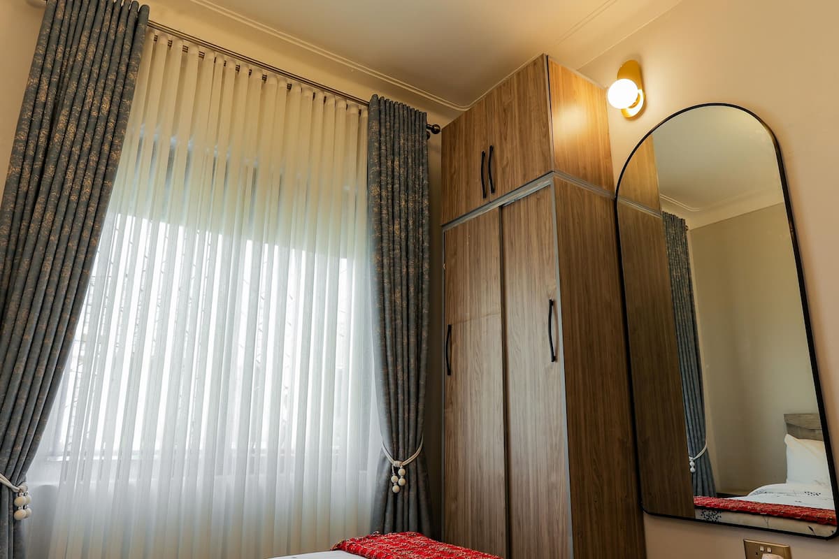 A bedroom with a bed, a wardrobe, a mirror, and a window with curtains.