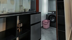 Een compacte keuken met zwarte kastjes, een glazen plank met keukengerei, een koelkast en een wasmachine.