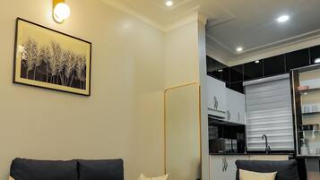 A modern living room with a black leather sofa, a glass coffee table, and a kitchen in the background.