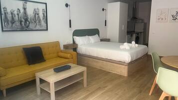 Una habitación de hotel compacta con una cama, un sofá, una mesita y una silla.