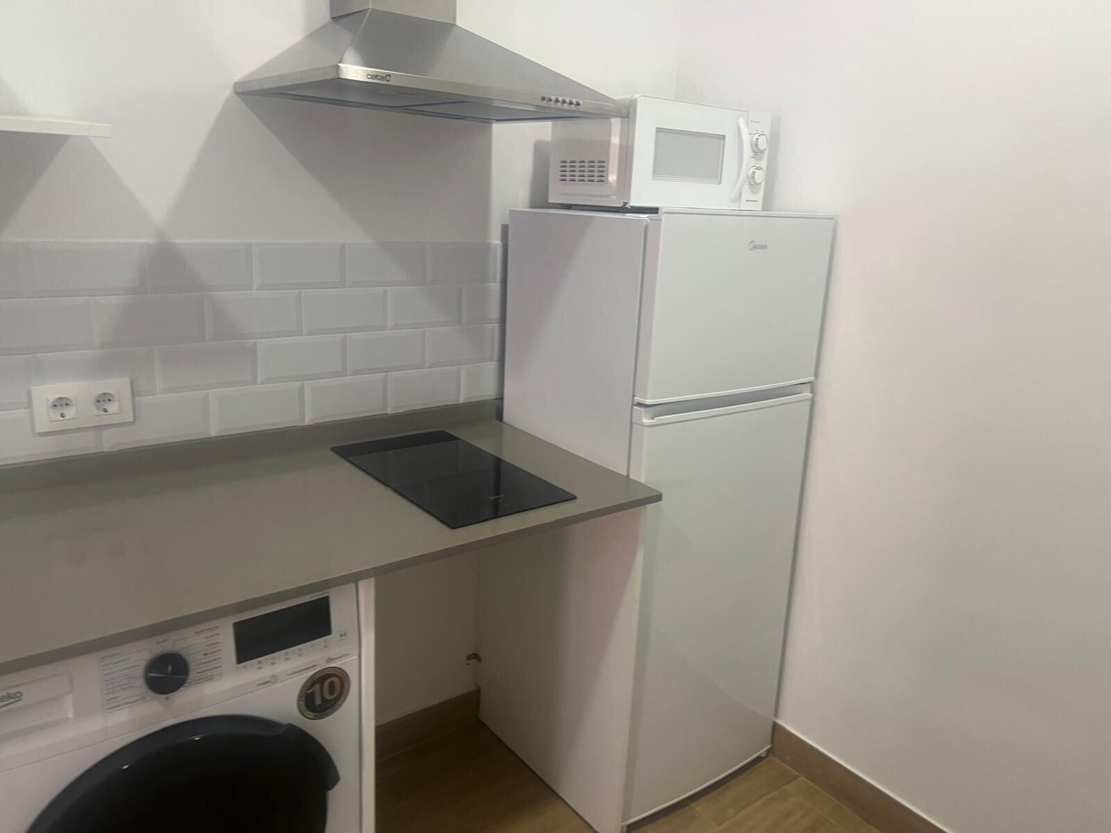Una cocina compacta equipada con microondas integrado, campana extractora de acero inoxidable, lavadora y refrigerador.
