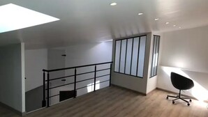 Una habitación amplia con techo inclinado, una silla de oficina negra y suelo de madera.