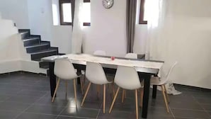 Un comedor con una mesa larga y seis sillas, una escalera a la izquierda, y un reloj en la pared.