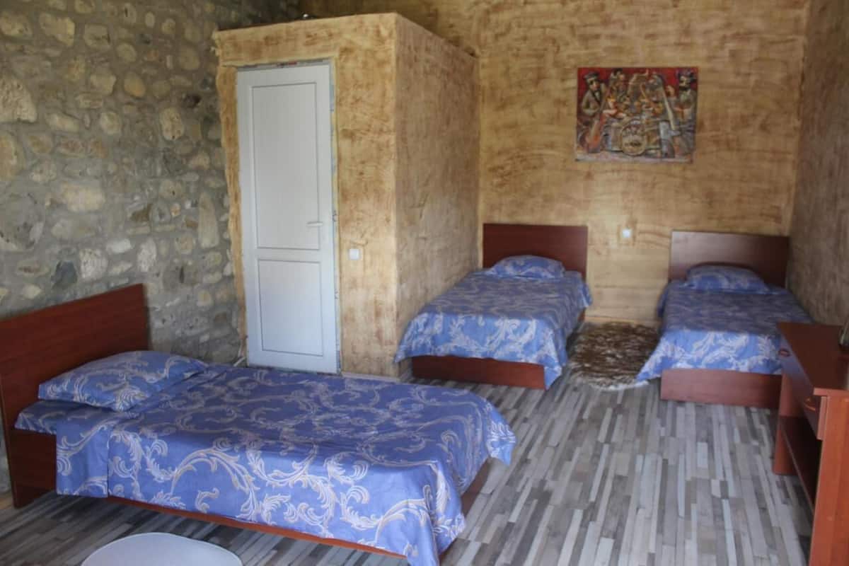 A room with three wooden beds, a stone wall, a wooden door, and a painting on the wall.