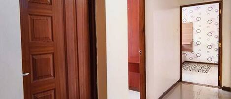 Un couloir avec une porte en bois, un sol carrelé et un mur orné d’un motif.