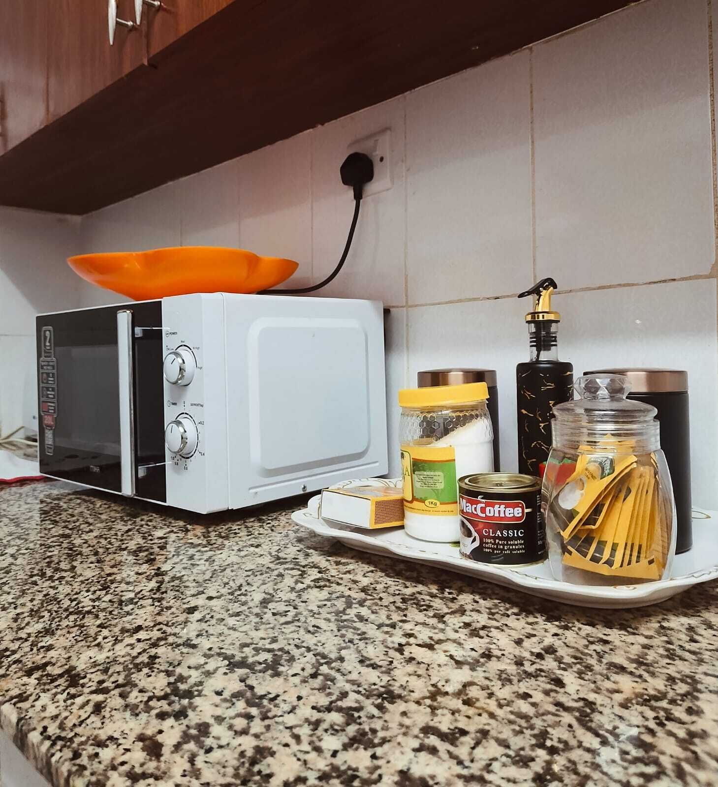 A kitchen with a microwave, a coffee maker, and various food items on the counter.
