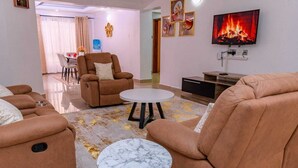 Ein modernes Wohnzimmer mit einem braunen Sofa, einem weißen runden Tisch und einem Fernseher, der ein Feuer zeigt.