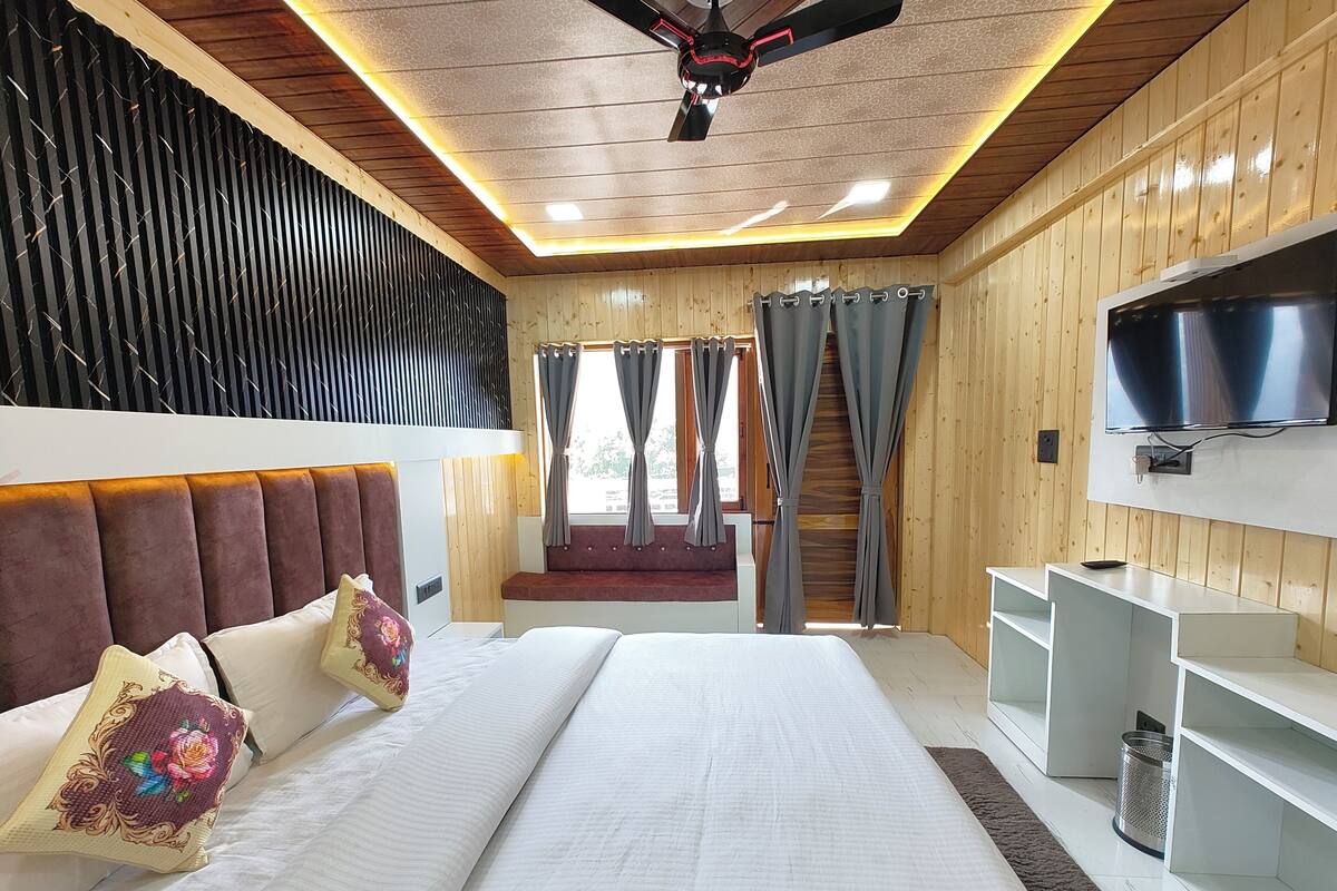 Ein modernes Schlafzimmer mit einem großen Bett, einem Deckenventilator, einem Fernseher und einem Fenster mit Vorhängen.